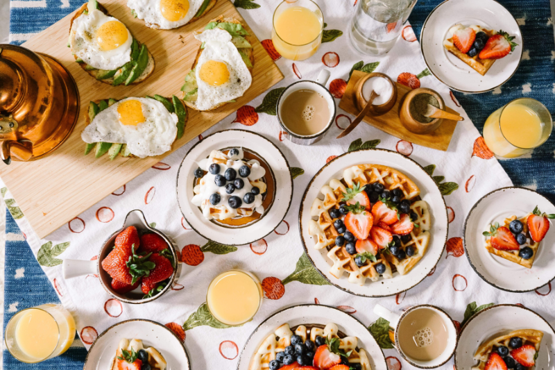 tavolo imbandito per un brunch con waffle alla frutta, bruschette con uova e avocado e caffelatte